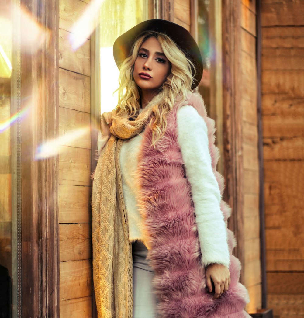standing woman in pink fur vest beside house wall