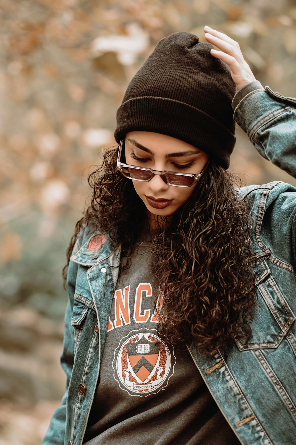 woman wearing blue denim jacket touching her hat while standing and looking down