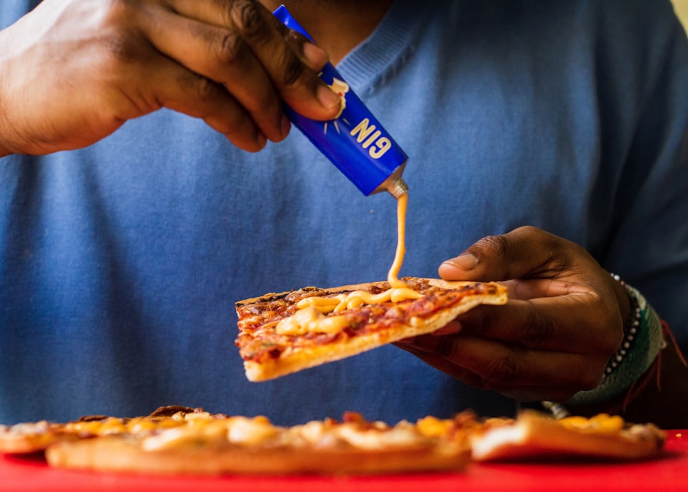 person putting mustard on pizza slice