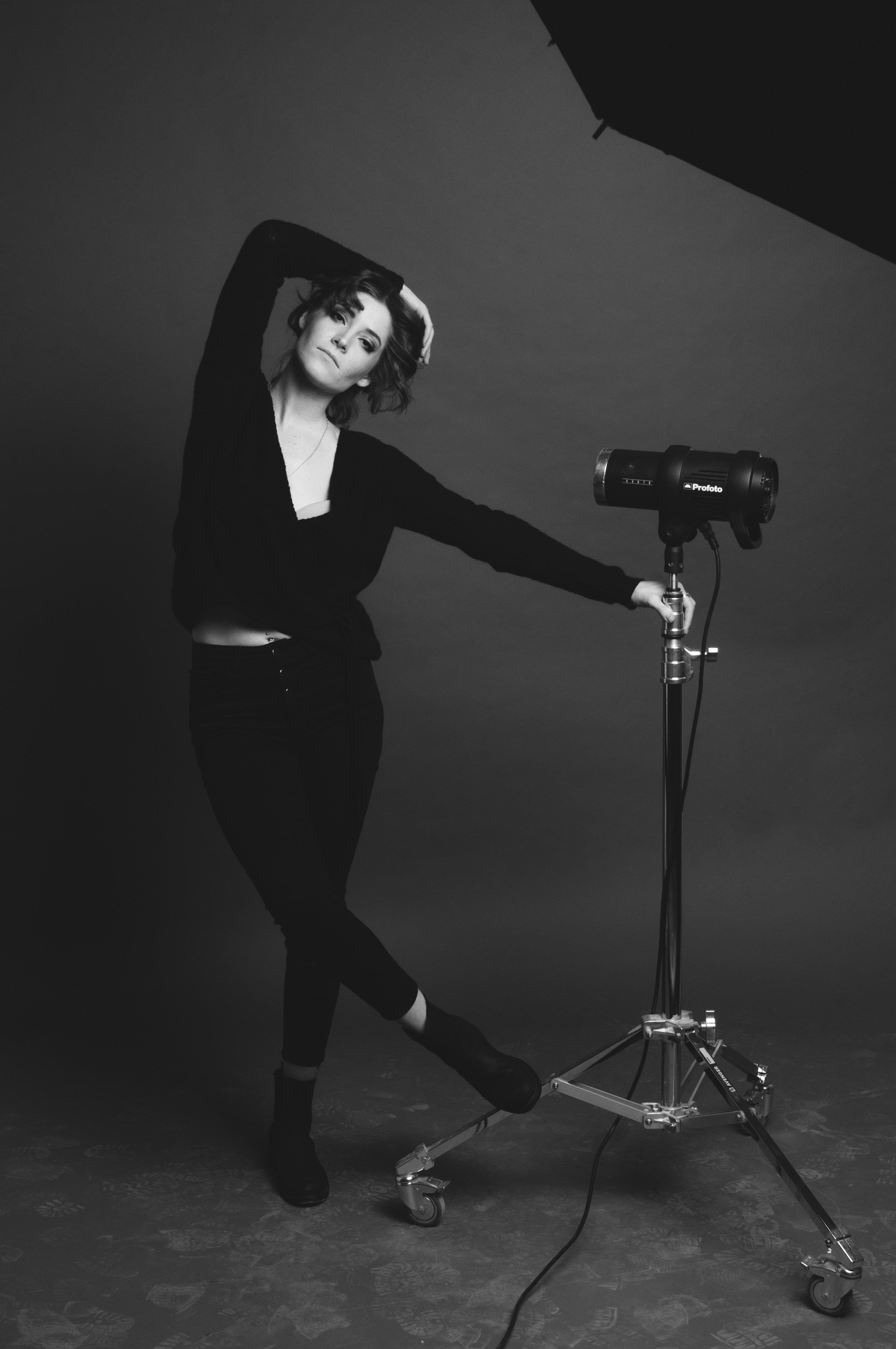 Female photographer with direct gaze in a dark moody portrait studio with single overhead spotlight