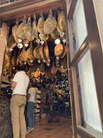 Artisan carefully inspecting a hanging Iberian ham in a traditional curing cellar with rustic wooden beams.