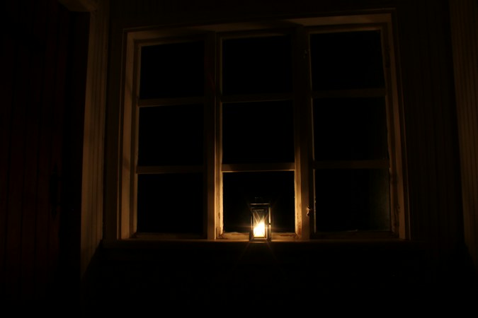 A single lit candle on a windowsill in a darkened room, the kind of light households fall back on when the power goes out