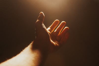 Close-up of hands raised in worship, bathed in soft natural light with earthy tones.