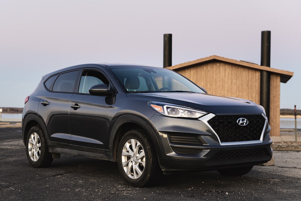 black Hyundai vehicle beside beige wooden house at daytime