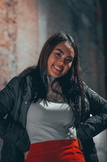 A young woman confidently posing in a fashionable, urban outfit against a vibrant backdrop.