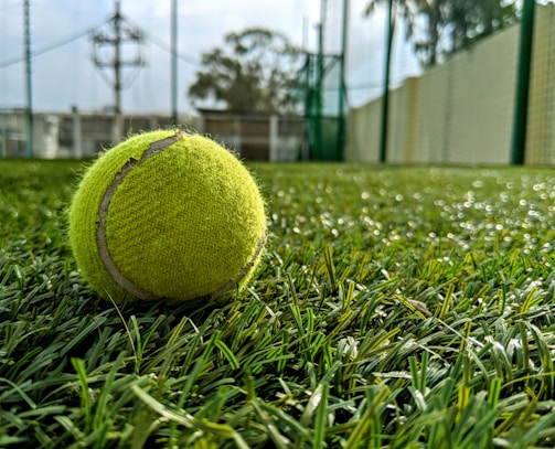 A close-up of a tennis racket hitting a bright yellow ball mid-air on a sunny court.