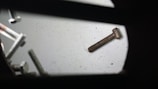 An assortment of metal screws scattered on a flat surface, with both shiny and rusty screws visible. A prominent rusty screw lies detached from the group, emphasizing age and usage contrast.