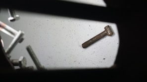 An assortment of metal screws scattered on a flat surface, with both shiny and rusty screws visible. A prominent rusty screw lies detached from the group, emphasizing age and usage contrast.