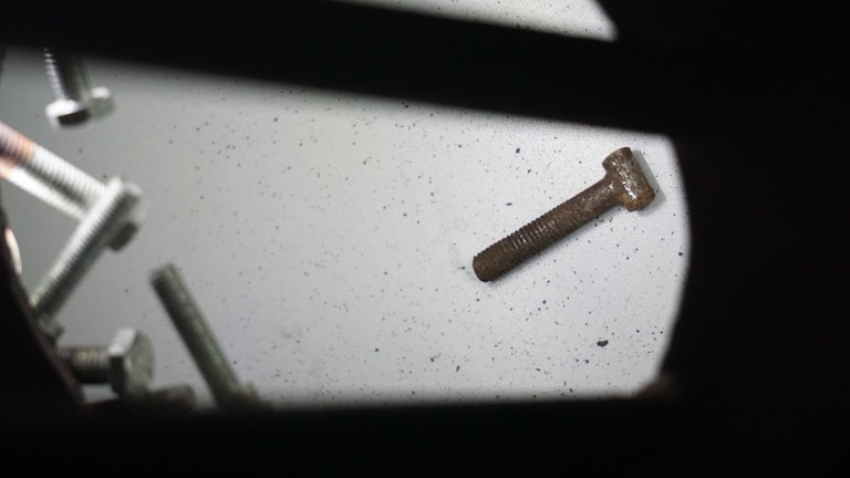 An assortment of metal screws scattered on a flat surface, with both shiny and rusty screws visible. A prominent rusty screw lies detached from the group, emphasizing age and usage contrast.