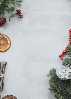 red fruits beside pine leaves and sliced fruit on white surface