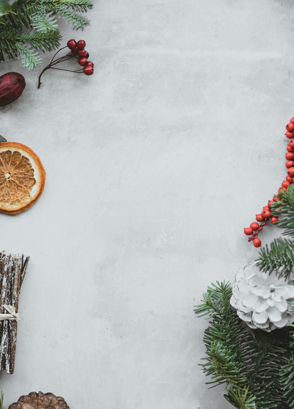 red fruits beside pine leaves and sliced fruit on white surface