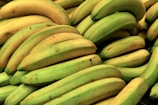 A large pile of ripe and unripe bananas, displaying various shades of yellow and green. The bananas are closely stacked, with some showing minor blemishes and spots.