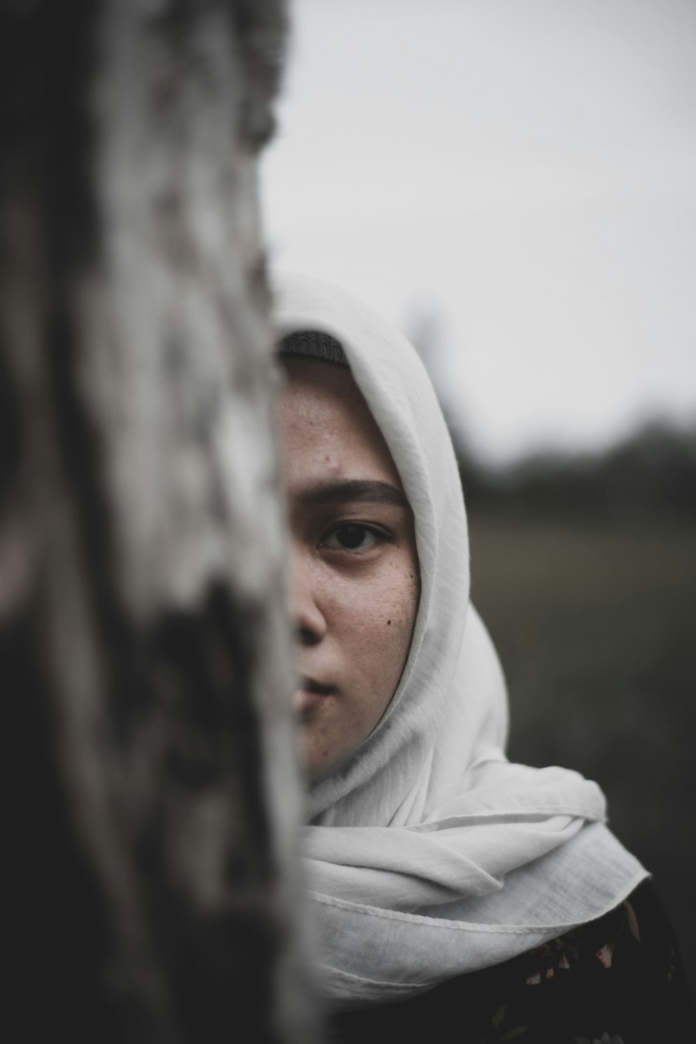 a woman wearing a white head scarf standing next to a tree