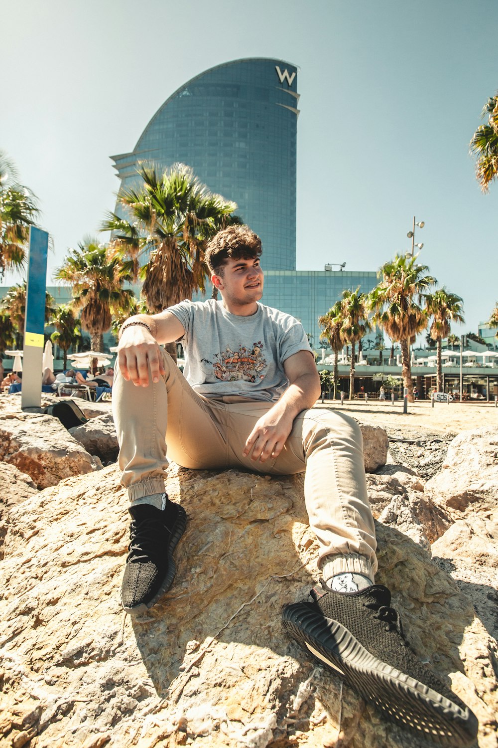 Mann mit grauem T-Shirt in brauner Hose sitzt auf Felsen