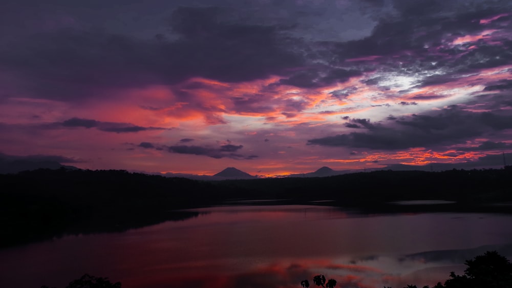 body of water viewing mountain under orange and blue sky