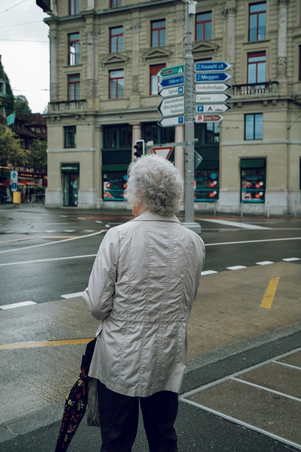 woman wearing grey jacket carrying umbrella standing on street