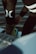 A person is putting on or adjusting water sports gear, standing on a platform above a body of water. The lower part of their body is visible, dressed in a black wetsuit with prominent white logos. Their footwear appears specialized, suggesting activities like wakeboarding or water skiing.