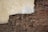A weathered brick wall with patches of peeling plaster and exposed masonry, showcasing a blend of rough and smooth textures. The plaster has worn away in several areas, revealing the uneven and aged bricks beneath.
