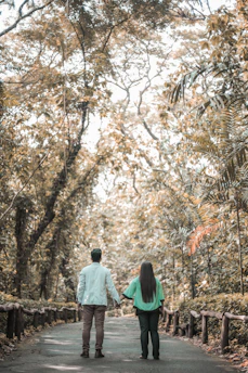 A cozy couple holding hands while walking through a sunlit forest path.