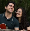 selective focus photography of smiling woman beside man who play guitar during daytime