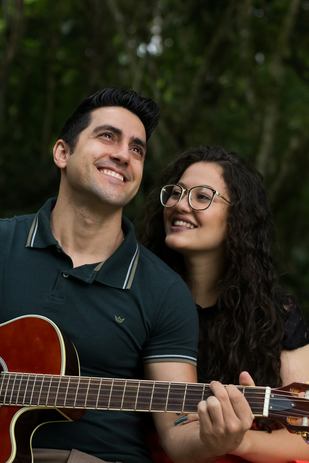 Selektive Fokusfotografie einer lächelnden Frau neben einem Mann, der tagsüber Gitarre spielt
