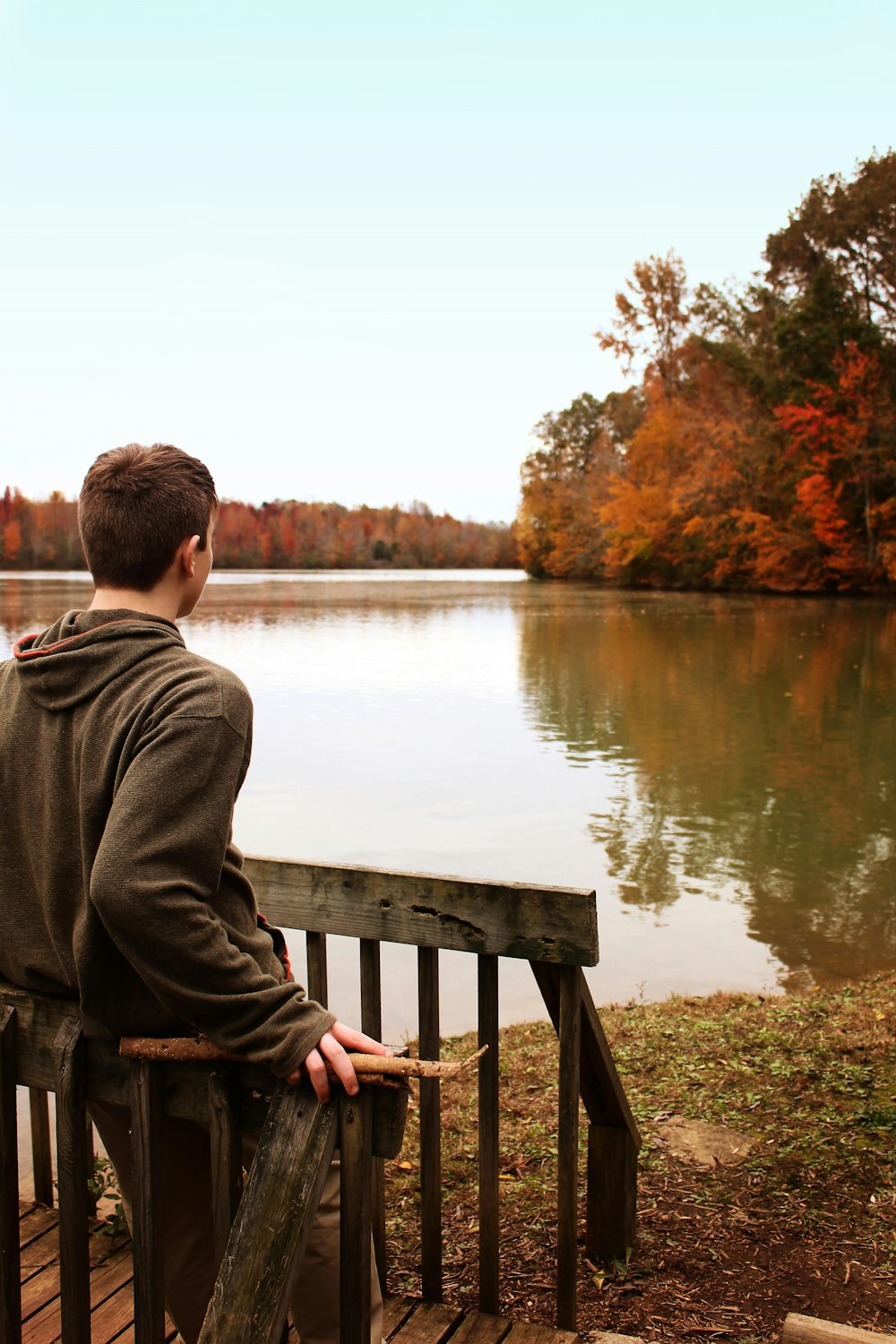 man leaning on wooden fence while facing on lakeshore during daytime