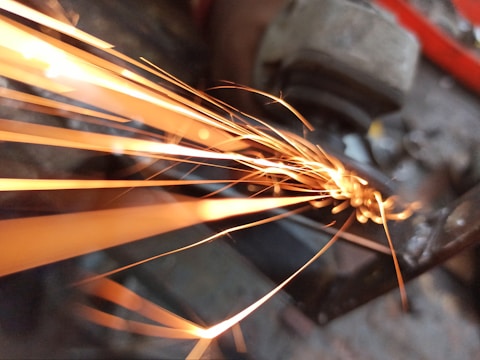 Stack of steel beams with sparks flying from a grinder in the background.