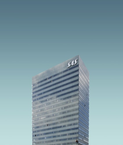 A tall, modern skyscraper with reflective windows and the letters 'SAS' displayed at the top. The building stands against a clear, cloudless sky.