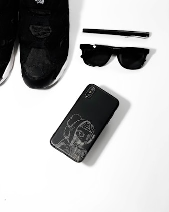 A collection of black accessories including watches, belts, and sunglasses on a matte black surface