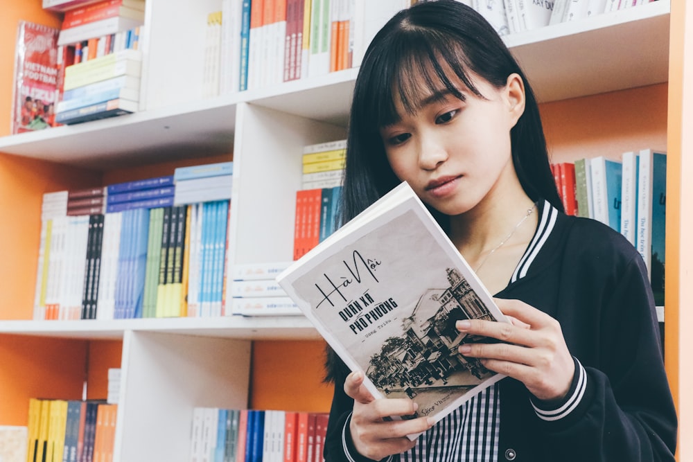 a woman reading a book in front of a bookshelf