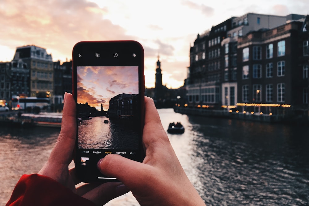 person taking picture of canal and tower