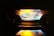 A close-up view of a gas stove burner with a bright blue flame, accented by hints of orange and yellow. The metal components of the burner are visible around the flame, and the surrounding area is dimly lit.