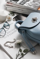 gray leather handbag beside eyeglasses and books