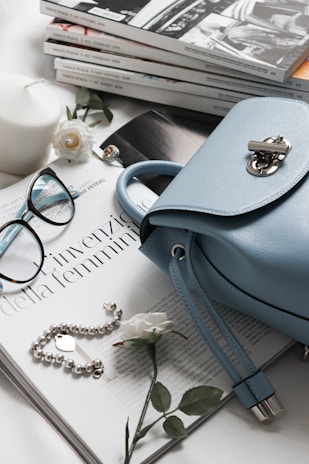 gray leather handbag beside eyeglasses and books