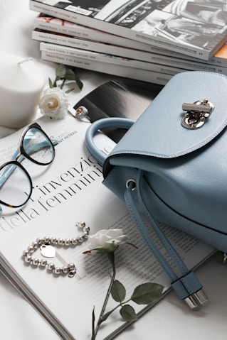 gray leather handbag beside eyeglasses and books