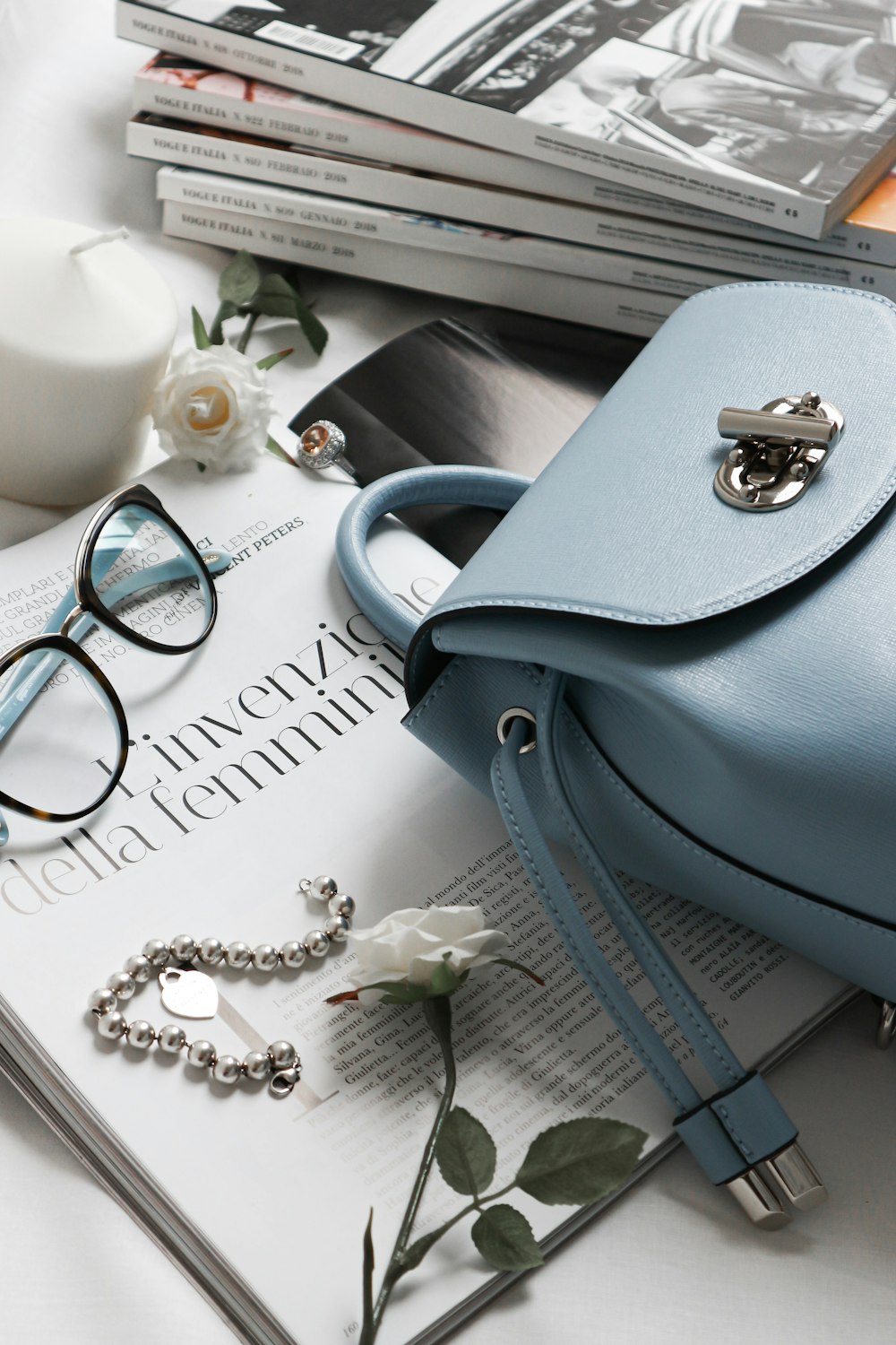 gray leather handbag beside eyeglasses and books