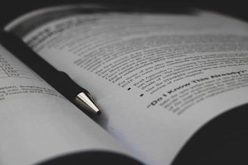 An open book with printed text visible on the pages, accompanied by a black pen resting diagonally across one of the pages. The text includes bullet points and appears to be educational material.