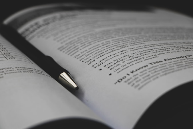 An open book with printed text visible on the pages, accompanied by a black pen resting diagonally across one of the pages. The text includes bullet points and appears to be educational material.