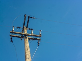 A utility pole with several wires and insulators set against a clear blue sky. The structure is constructed of wood and metal components, with multiple cables extending outward.