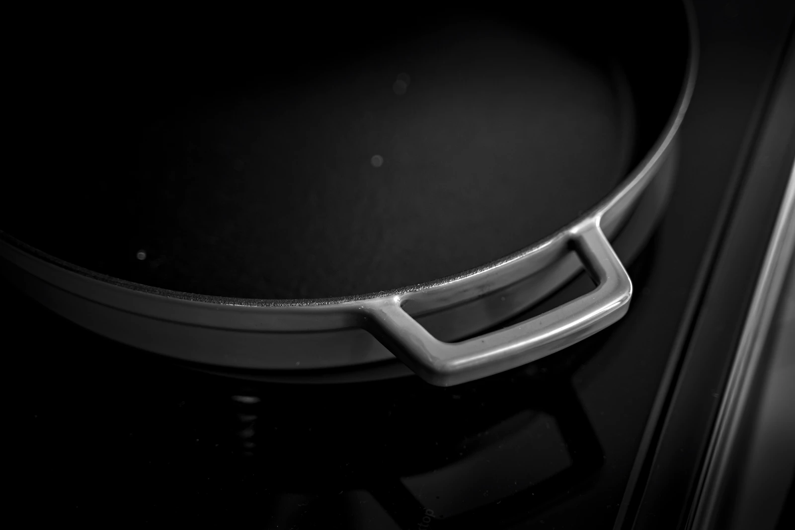 Low-key detail of a black braiser rim and silver loop handle