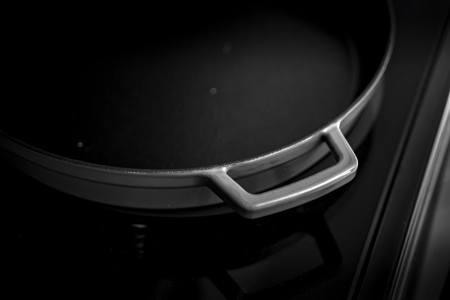 Low-key detail of a black braiser rim and silver loop handle