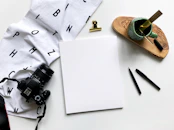 A creative flat lay of design sketches, color swatches, and a camera on a wooden desk.
