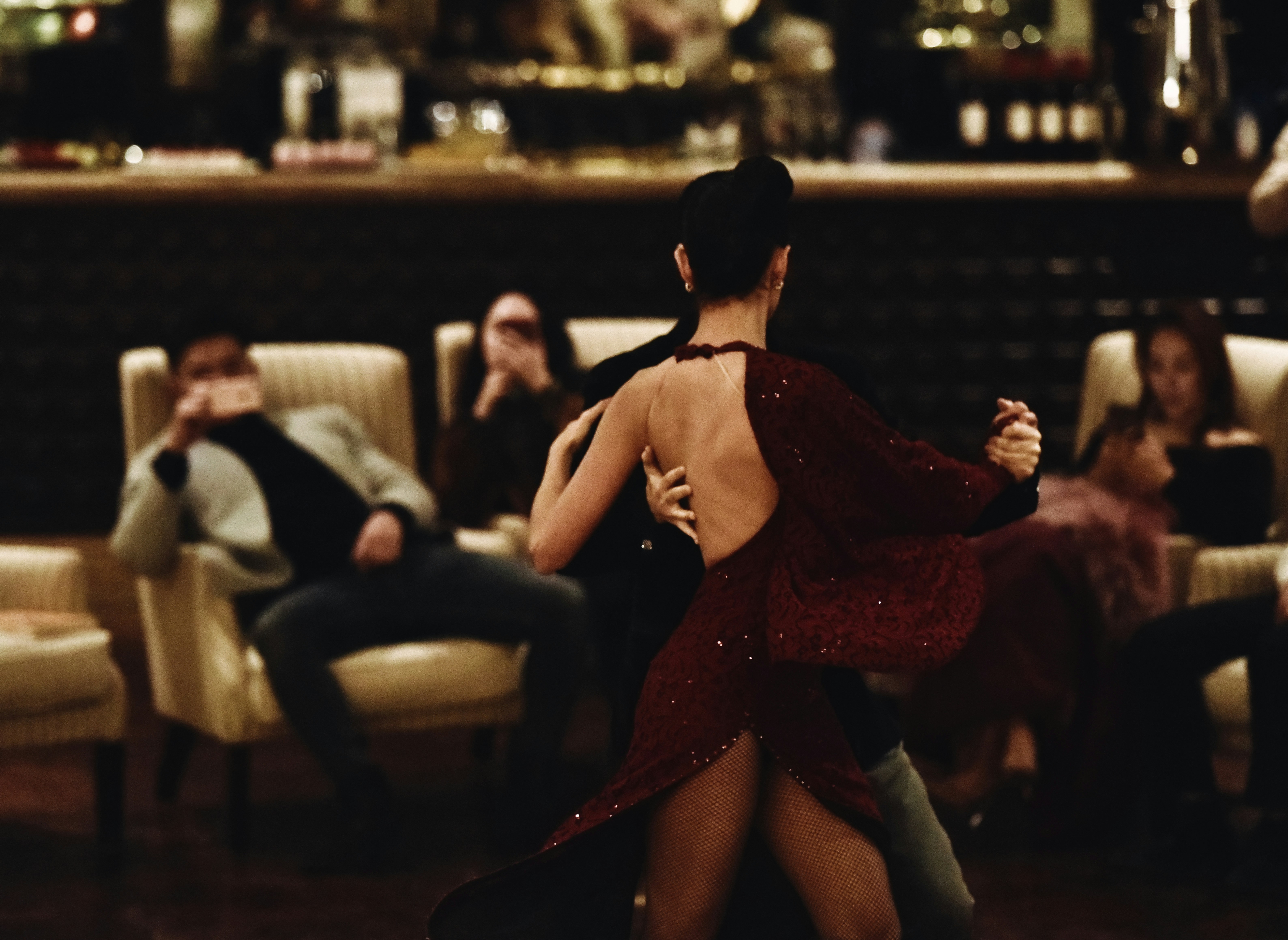 Dancers perform tango in dimly lit room with red dress.