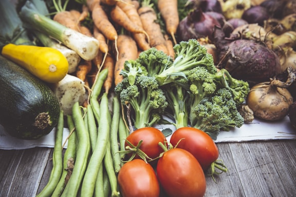 A vibrant assortment of fresh vegetables including green beans, carrots, tomatoes, potatoes, onions, and bell peppers arranged on a rustic wooden table.