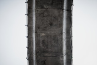 A close-up view of the underside of a large concrete bridge or overpass structure. The image features details of the concrete texture and support beams.
