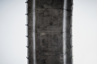 A close-up view of the underside of a large concrete bridge or overpass structure. The image features details of the concrete texture and support beams.