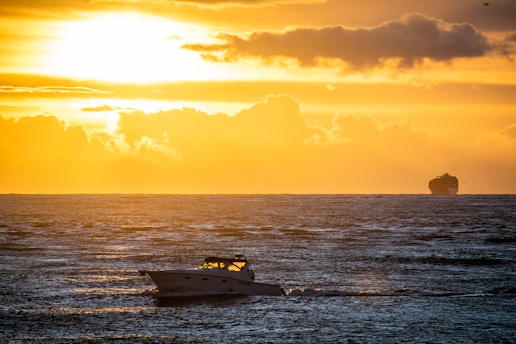 A vibrant sunset over a vast ocean with a cargo ship sailing steadily.