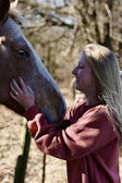 Close-up of a smiling volunteer gently brushing a horse’s mane surrounded by nature.