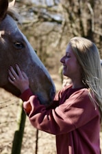 A smiling rider with a volunteer leading a calm horse in a sunlit paddock.