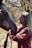 A person with long blonde hair is smiling while gently touching the face of a brown horse. They appear to be in a natural outdoor setting with blurred trees in the background.